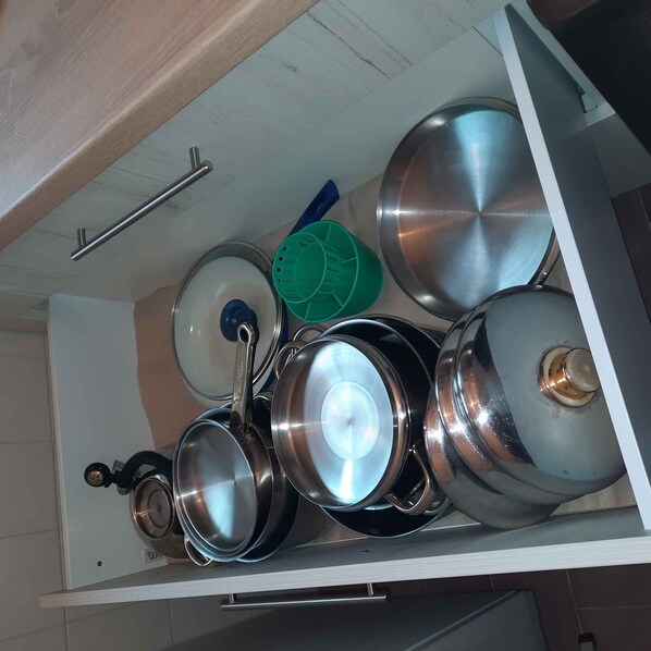 A kitchen drawer with various pots and pans, a green colander, and a metal handle.