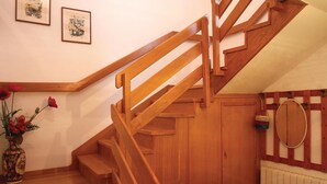 Eine Holztreppe mit Handlauf, eine Vase mit roten Blumen und ein gerahmtes Bild an der Wand.