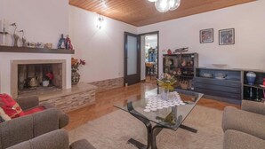 Ein geräumiges Wohnzimmer mit Kamin, einem Glastisch und einem Essbereich, der durch eine offene Tür sichtbar ist.