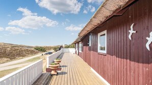 Een houten terras met een gebouw met rieten dak, witte hekwerk en potplanten.