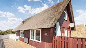 Een rieten hut met een houten terras en een witte omheining.