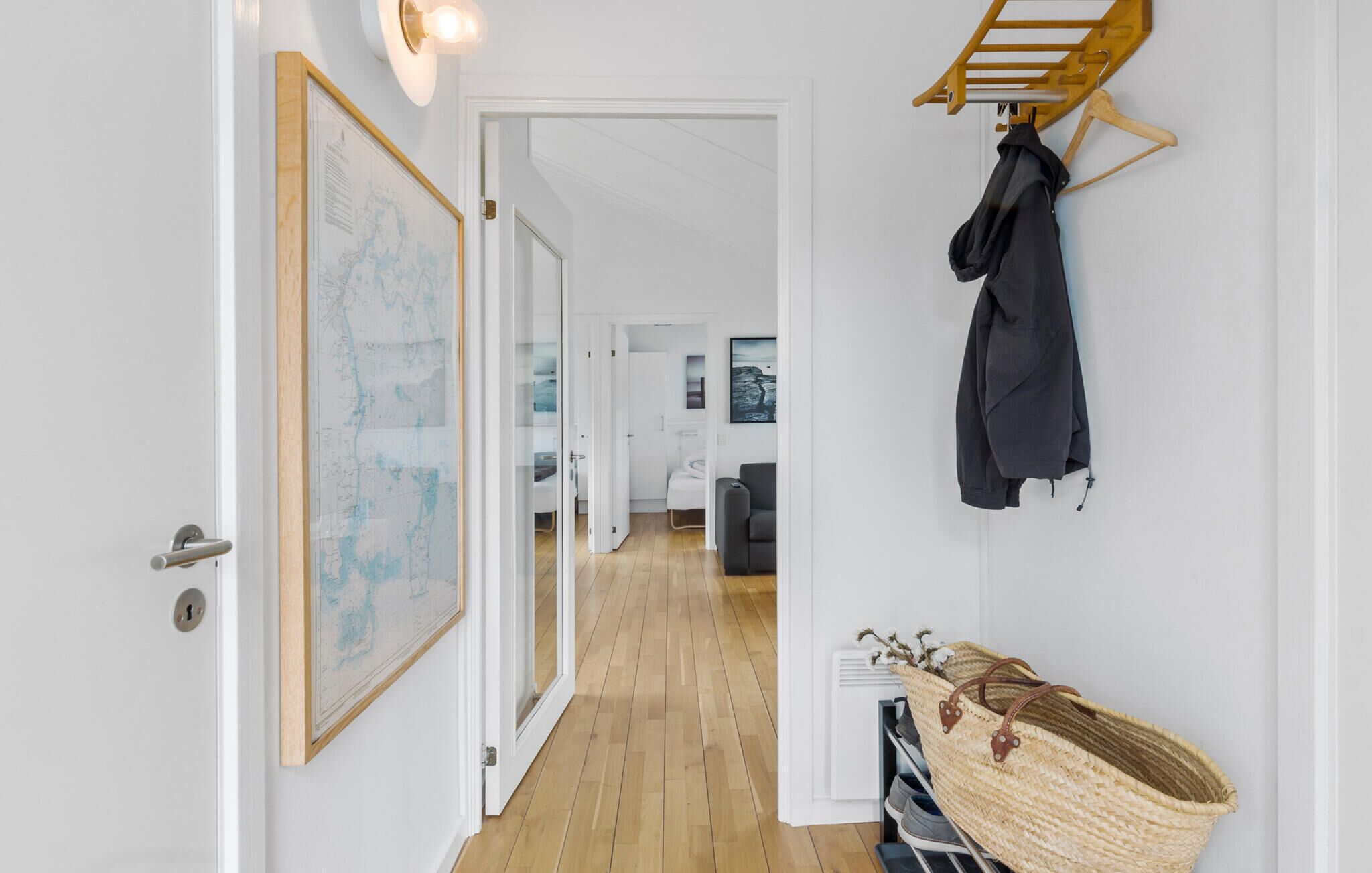 A hallway with a wooden floor, a map on the wall, a coat rack with a jacket, and a basket with shoes.