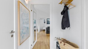 Een gang met houten vloer, een kaart aan de muur, een kapstok met jas en een mand met schoenen.