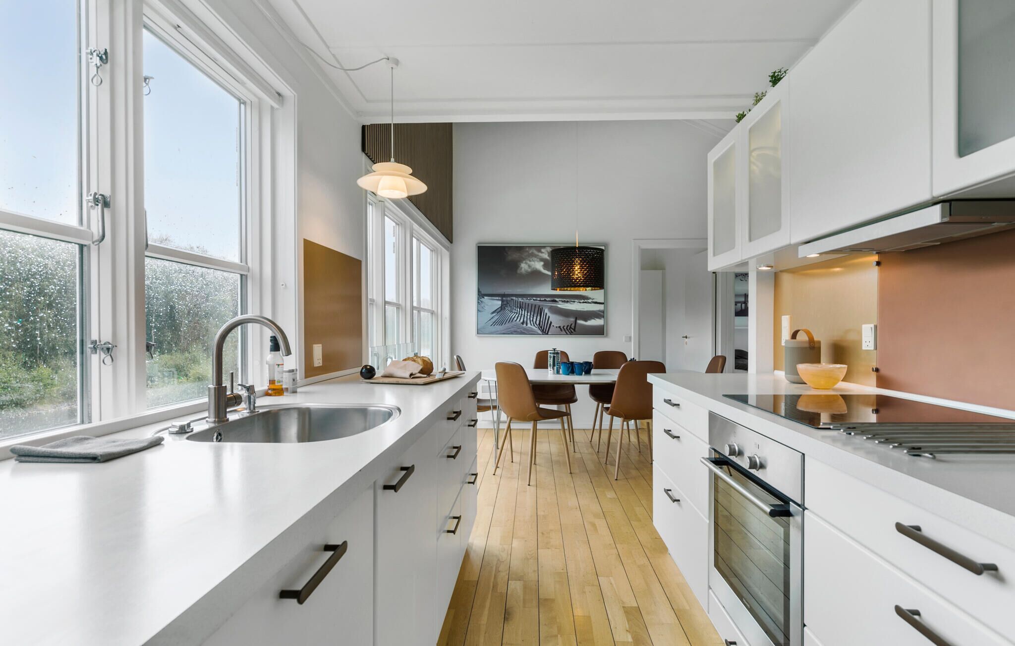 A modern kitchen with white cabinetry, a large window, and a dining area with a table and chairs.