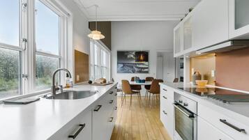 A modern kitchen with white cabinetry, a large window, and a dining area with a table and chairs.