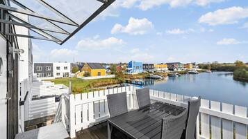 A riverside view from a deck with a table and chairs, overlooking colorful houses and boats on the water.