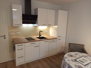 Une cuisine compacte avec des meubles blancs, un plan de travail en bois, un évier noir et une hotte intégrée.