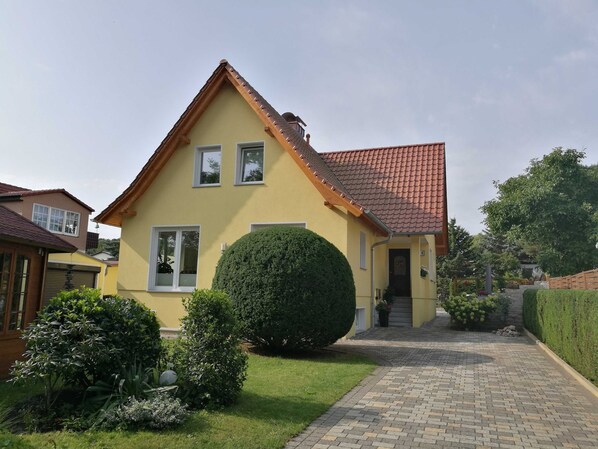 Une maison jaune avec un toit recouvert de tuiles rouges, une pelouse bien entretenue et une allée pavée.