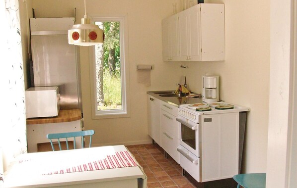 A compact kitchen with white cabinets, a sink, a stove, and a window with a view of trees. - 2 bedroom cozy home in Torsås (Torsås)