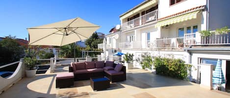 A rooftop patio with outdoor furniture, a large umbrella, and a white building with balconies.