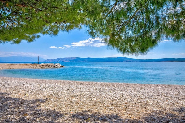 A pebble beach with a clear view of the sea and distant mountains.