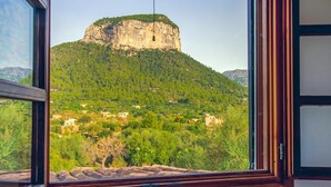 Blick durch ein Fenster auf eine gebirgige Landschaft mit einer markanten Felsformation und verstreuten Gebäuden.