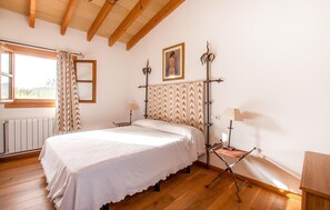 Un dormitorio con cama, ventana con cortinas, radiador, un cuadro en la pared y una lámpara.