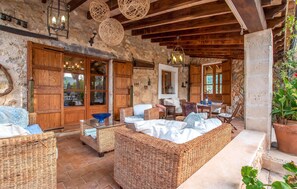 Un interior rústico con muebles de mimbre, paredes de piedra, vigas de madera y un comedor con mesa y sillas.