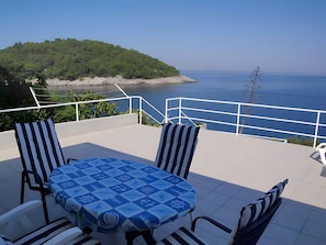 Een terras met een tafel en stoelen, met uitzicht op de kust en een heuvel op de achtergrond.