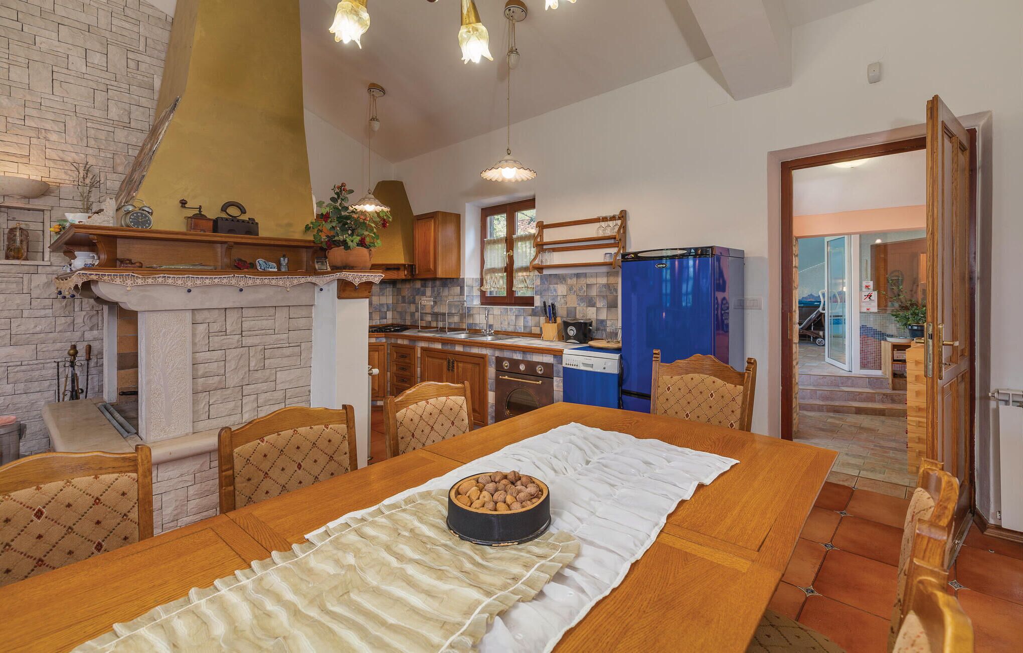 A cozy kitchen with a dining area, featuring a stone fireplace, wooden furniture, and a blue refrigerator.