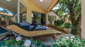 A covered outdoor seating area with a pool, cushioned lounge chairs, and potted plants. - Amazing home in Belavici with sauna (Belavici)