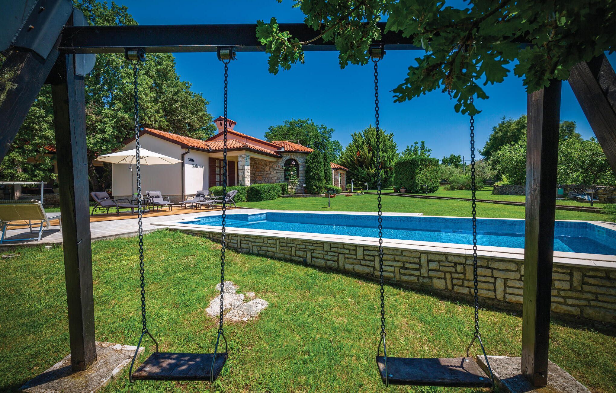 Ein Garten mit Swimmingpool, Schaukel und einem Haus mit rotem Dach.