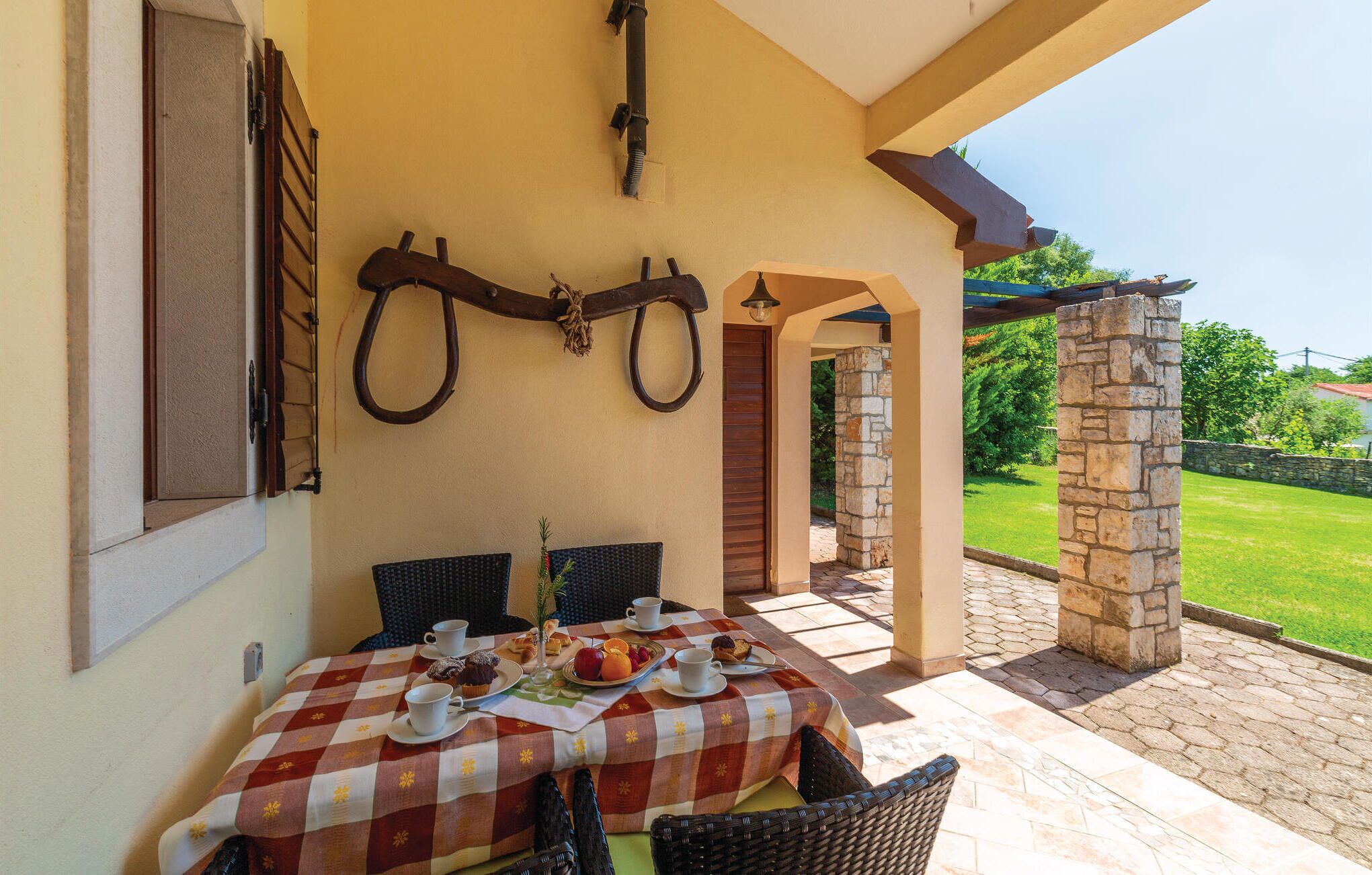 A covered outdoor dining area with a checkered tablecloth, wicker chairs, and a stone pillar.