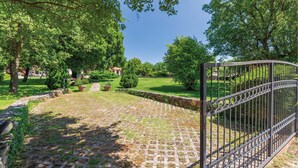 A paved pathway leading to a gated entrance in a park-like setting with trees and a lawn. - Amazing home in Belavici with sauna (Belavici)