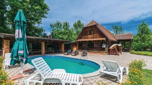 Una cabaña de madera con piscina, rodeada de un patio de ladrillo y mobiliario exterior.