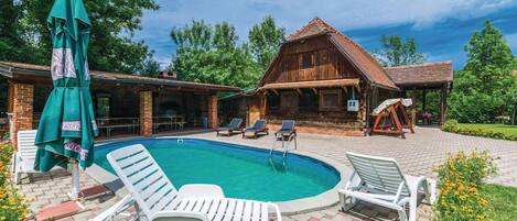 Una cabaña de madera con piscina, rodeada de un patio de ladrillo y mobiliario exterior.