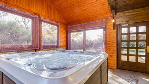 Una cabaña de madera con jacuzzi, ventanas amplias y vista a una piscina exterior.