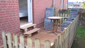 A wooden deck with a table and chairs, a wooden fence, and a brick wall. - Ankerplatz Vacation Rental - - Ankerplatz Vacation Rental (Brodersby)