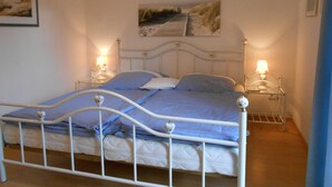 A bed with a metal frame, two bedside tables with lamps, a painting above the bed, and a small shelf on the wall. - Ankerplatz Vacation Rental - - Ankerplatz Vacation Rental (Brodersby)