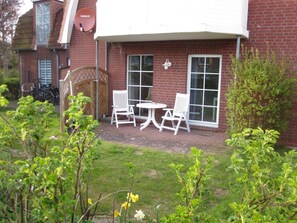 A brick house with a patio, white chairs, and a table.