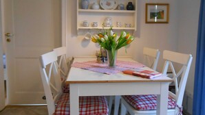A dining area with a white table, red and white checkered chairs, a vase with flowers, and a shelf with kitchenware. - Ankerplatz Vacation Rental - - Ankerplatz Vacation Rental (Brodersby)