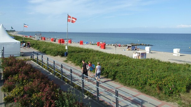 A coastal walkway with a flag, beach umbrellas, and a tent. - Ankerplatz Vacation Rental - - Ankerplatz Vacation Rental (Brodersby)