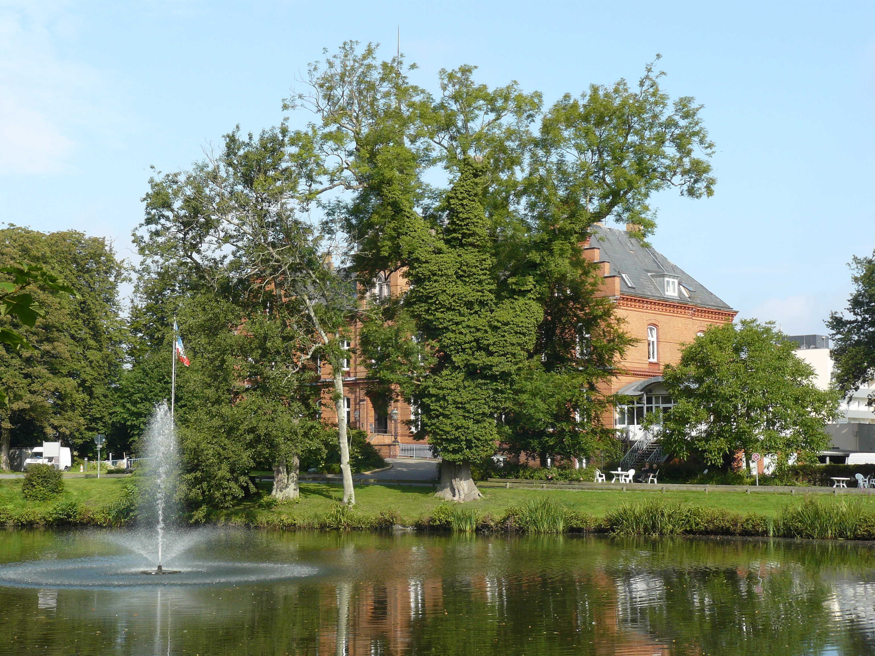 A building with a fountain in front, surrounded by trees and a pond.