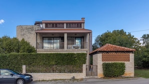 A two-story house with a balcony, a small attached structure with a tiled roof, and a stone wall.