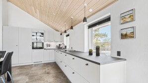 A modern kitchen with white cabinets, a large island, pendant lights, and a view of the outdoors.