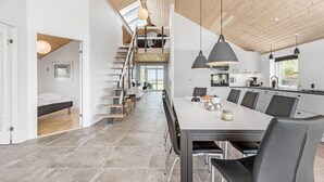 A modern kitchen with a central island, a dining area with a long table and chairs, and a staircase leading to an upper level.