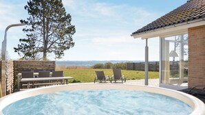 An outdoor swimming pool with lounge chairs and a table, overlooking a grassy area and the sea.