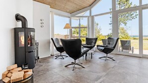 A modern living room with a wood-burning stove, comfortable seating, and large windows offering a view of the outdoors.