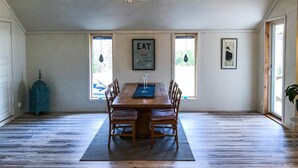 A dining area with a wooden table and chairs, framed artwork on the walls, and a blue decorative piece on the left.