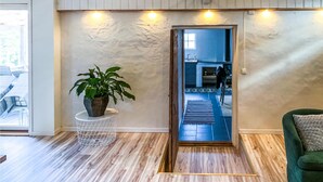 A room with a wooden floor, a green sofa, a potted plant, and a view into a kitchen area through a doorway.