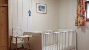 A baby room with a white crib, a wooden high chair, a small shelf with a toy, and a framed picture on the wall.