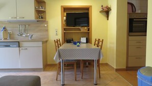 A compact kitchen with a dining table, chairs, and a TV mounted above it.