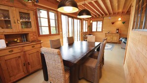 Interior de madera con una mesa de comedor, sillas y una zona de cocina con armarios y encimera.