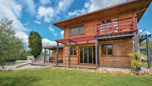 Una casa de madera de dos pisos con balcón, piscina y césped bien cuidado.