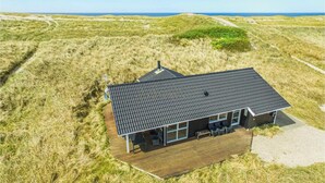 A modern house with a dark roof, large windows, and a wooden deck. - Nice home in Harboøre with sauna (Harboøre)