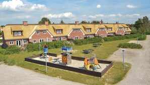 A row of traditional brick houses with thatched roofs, a playground with various play structures, and a gravel path leading to the houses. - 3 bedroom nice home in Blåvand (Blåvand)