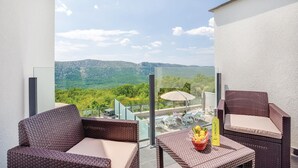 Een balkon met rieten meubilair, een glazen balustrade en uitzicht op een groen landschap.
