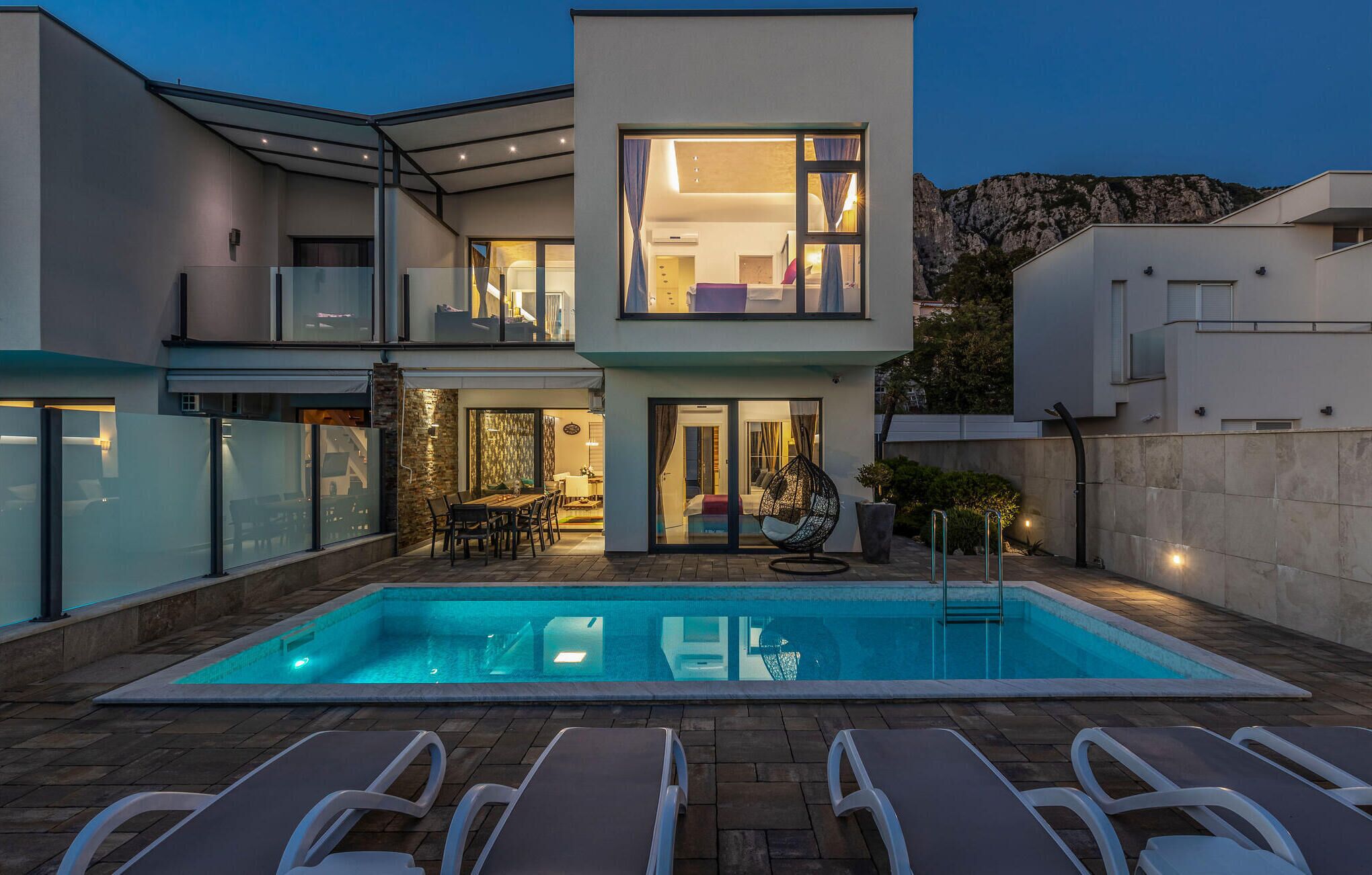 A modern two-story house with a swimming pool, outdoor seating, and a view of the surrounding landscape.