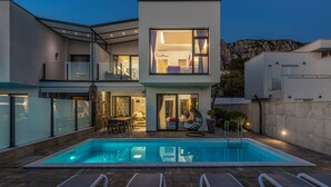 Een modern huis met twee verdiepingen, een zwembad, terras en uitzicht op het omliggende landschap.