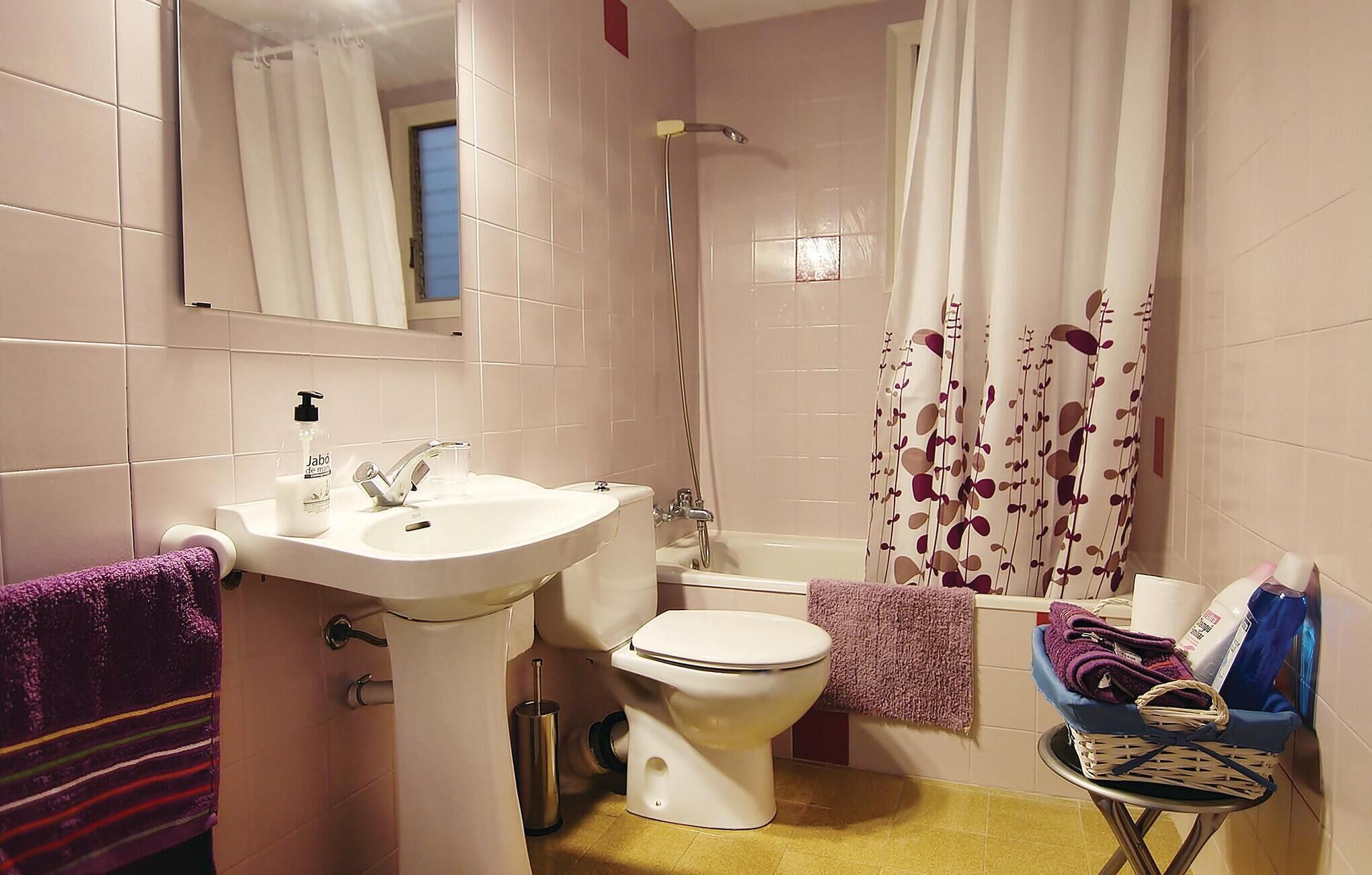 A bathroom with a sink, toilet, and bathtub. There is a towel rack with towels, a bottle of hand soap, and a basket with folded towels.